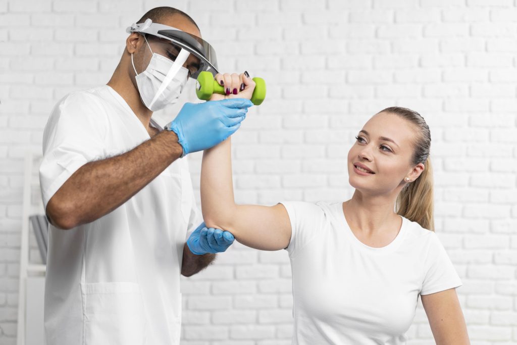 Sports medicine physician helps female patient with shoulder rehab using dumbbell during strength assessment in clinical setting.