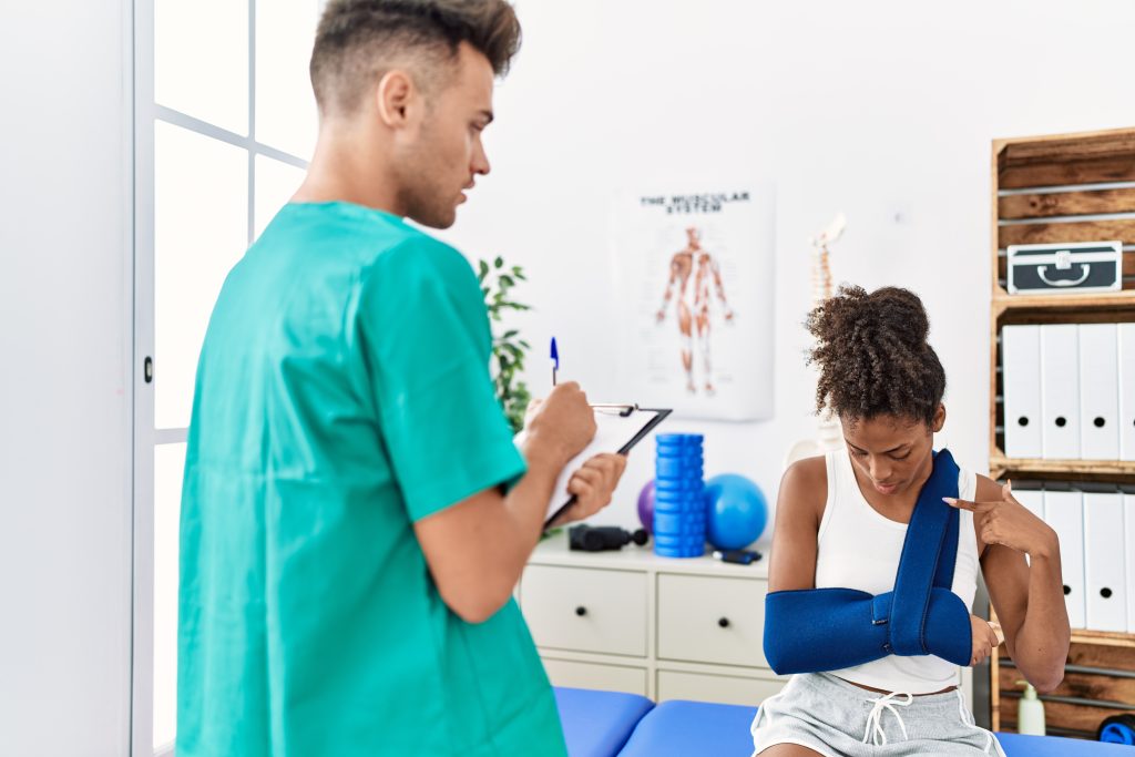 Injured woman consulting sports medicine physician during arm sling assessment in a physical therapy and rehabilitation clinic.