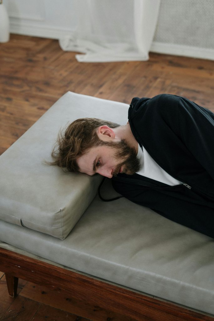Exhausted man lying on a mattress, symbolizing burnout and the need for lifestyle coaching with Dr. Pat Boulogne.
