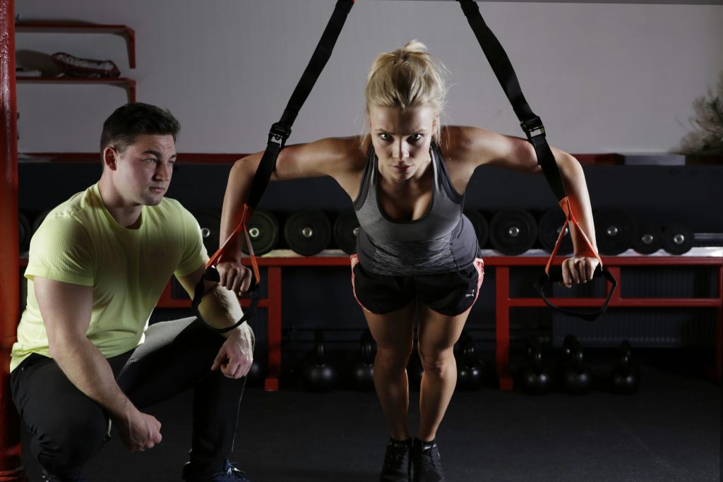 Focused woman in TRX workout with trainer support— personal nutritionist plan pairs fitness with nutritional balance.