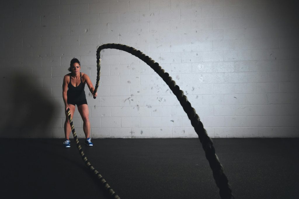 Woman doing battle ropes workout—personal trainer-style training promoted for strength and full-body fitness.